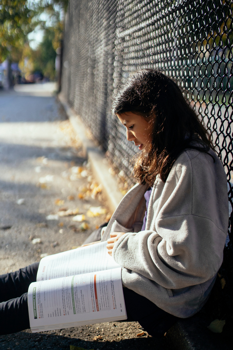 Teenage girl reading textbook on street